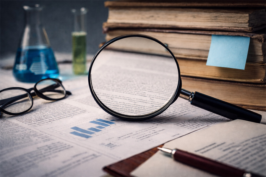 Méthodologie et esprit critique - Loupe posée sur des documents et des graphiques, entourée de livres et de matériel d’analyse.