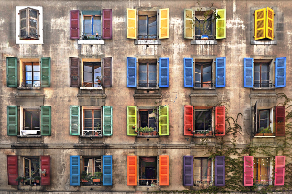 Façade d’un immeuble ancien dont les nombreuses fenêtres aux volets de couleurs différentes forment une mosaïque harmonieuse, symbole de la diversité des points de vue et des façons d’être.